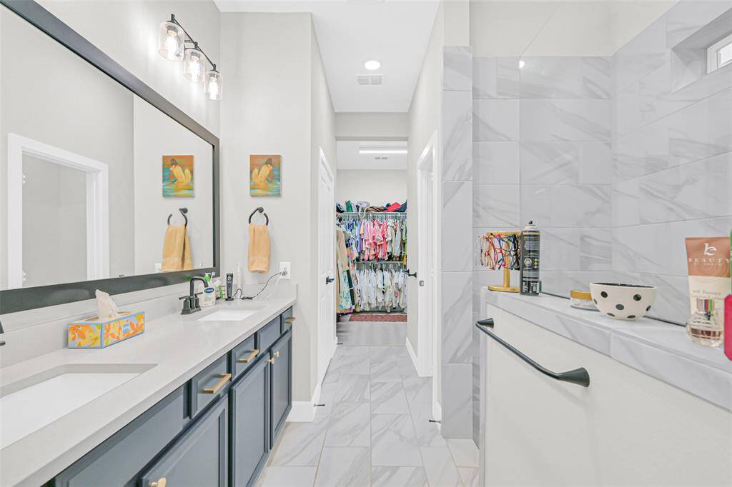 This spacious en-suite bathroom showcases a dual-sink vanity with striking blue cabinetry and elegant gold hardware, offering ample storage and direct access to a generous walk-in closet.