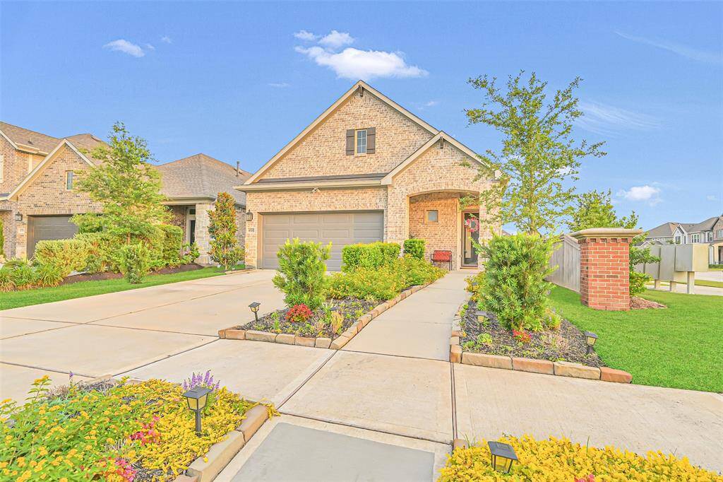 This stunning view highlights the immaculate curb appeal with lush, pristine landscaping surrounding the home. The exterior features modern brick and a spacious double-wide driveway that leads to a two-car garage.