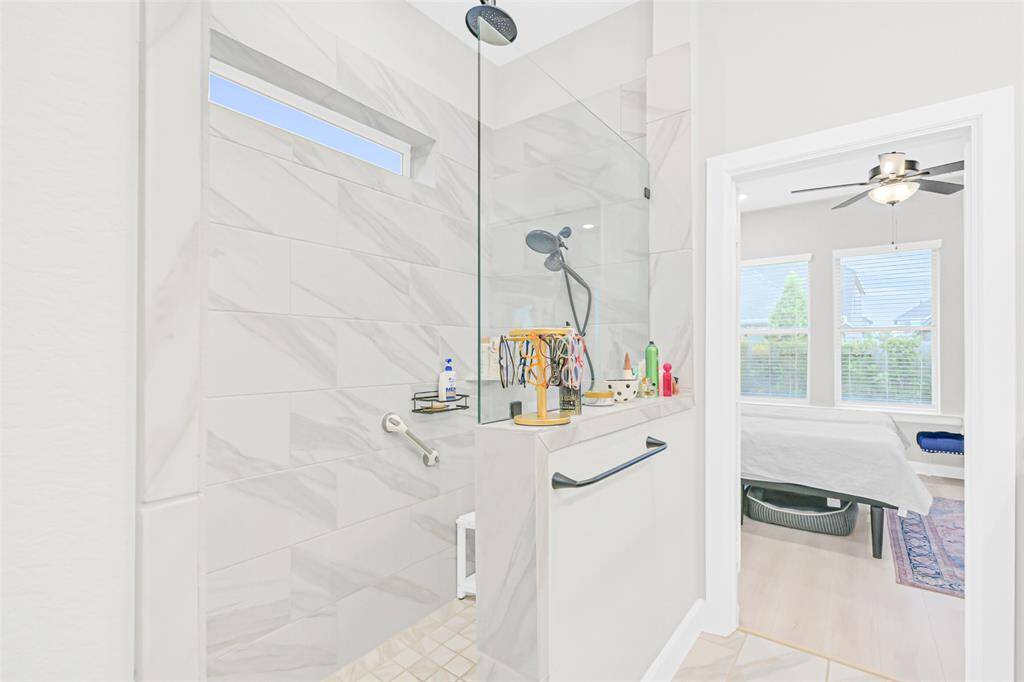 Step into a spa-inspired walk-in shower featuring elegant tilework, a built-in bench, and sleek black fixtures—seamlessly flowing into the bright and tranquil primary bedroom retreat.