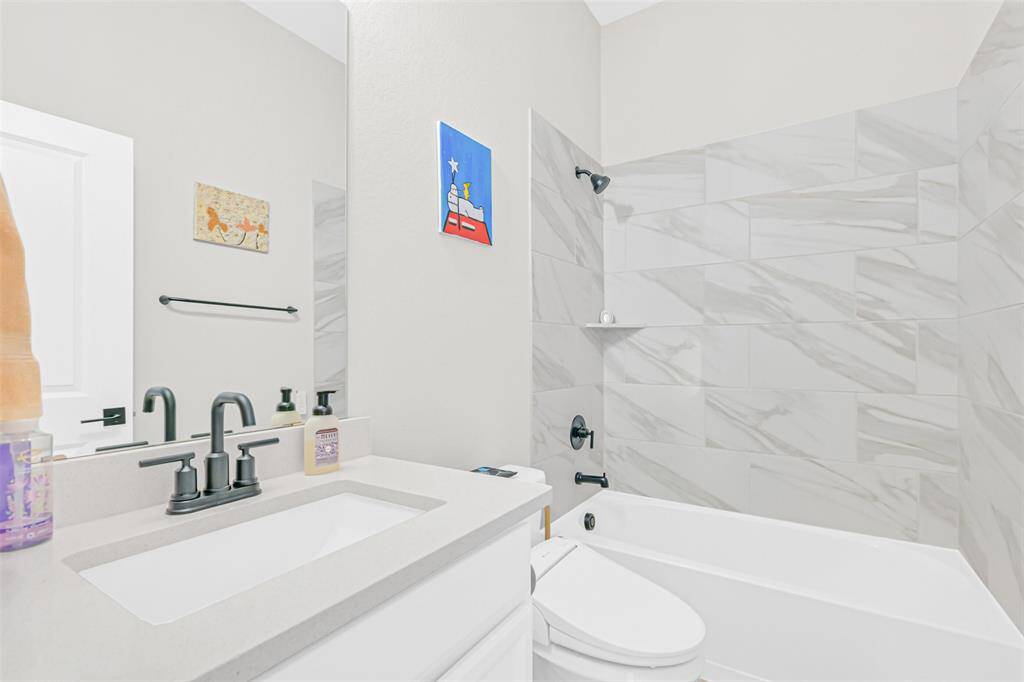 A modern secondary bathroom with sleek black fixtures, quartz vanity, and a tiled shower-tub combo—designed with both style and function in mind.
