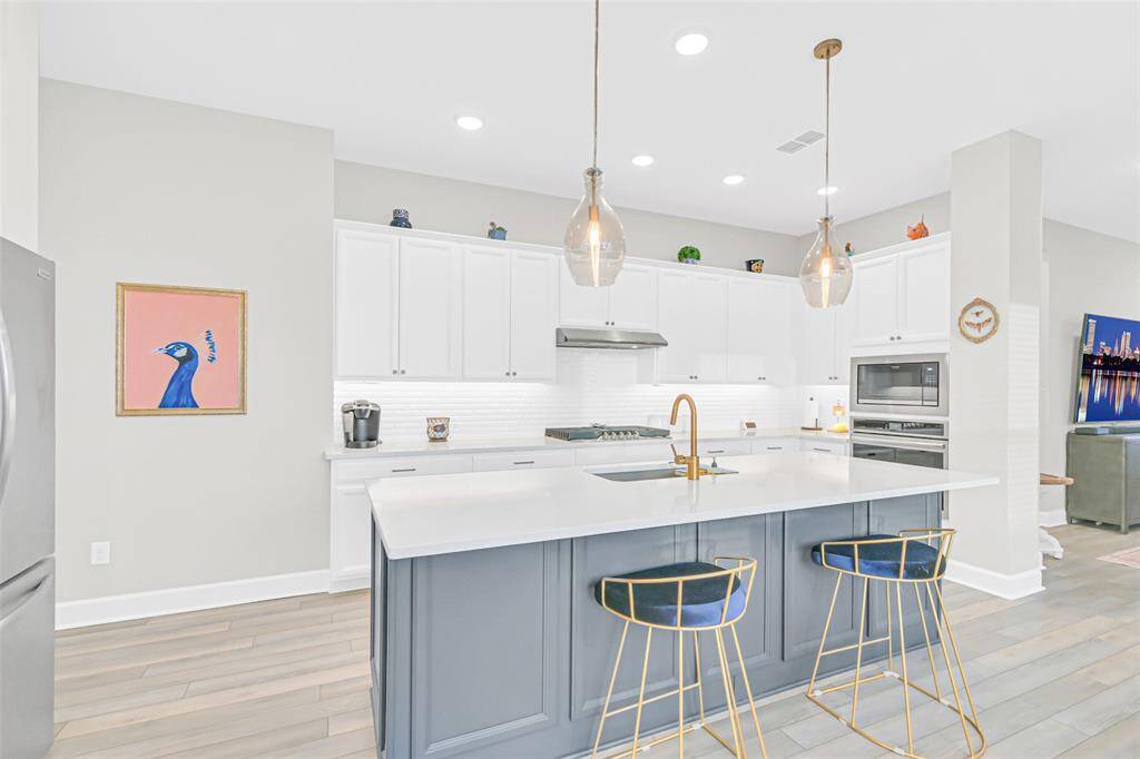 The chef’s kitchen is the heart of the home, featuring white shaker cabinetry, sleek stainless steel appliances, a separate island with breakfast seating, and a timeless white subway tile backsplash.