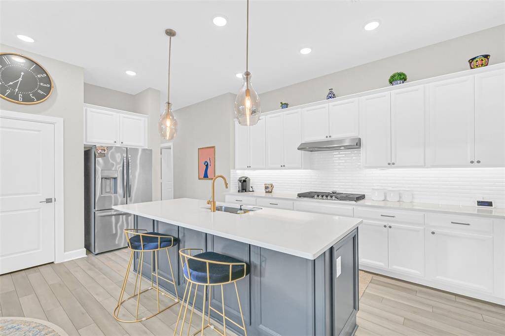 The generously sized kitchen island is illuminated by two modern pendant lights and sits perfectly between the kitchen and breakfast nook, offering abundant counter space for meal prep and casual breakfast seating.