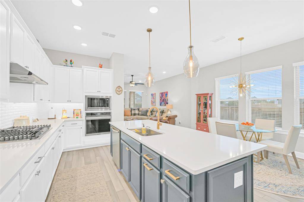 Bright and inviting, this open-concept kitchen features a striking contrast between crisp white cabinetry and a navy island with gold hardware, highlighted by elegant pendant lighting and natural light pouring through oversized windows.