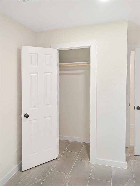 A well-lit, narrow hallway with light-colored walls and modern tile flooring. It features multiple doors leading to adjacent rooms, and a utility closet at the end housing a water heater.