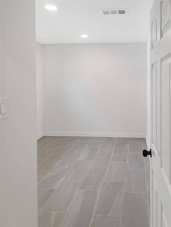 This photo shows a small, unfurnished room with light-colored tile flooring and neutral walls. It features recessed lighting and a white door with a black knob. Perfect for a home office or storage space.