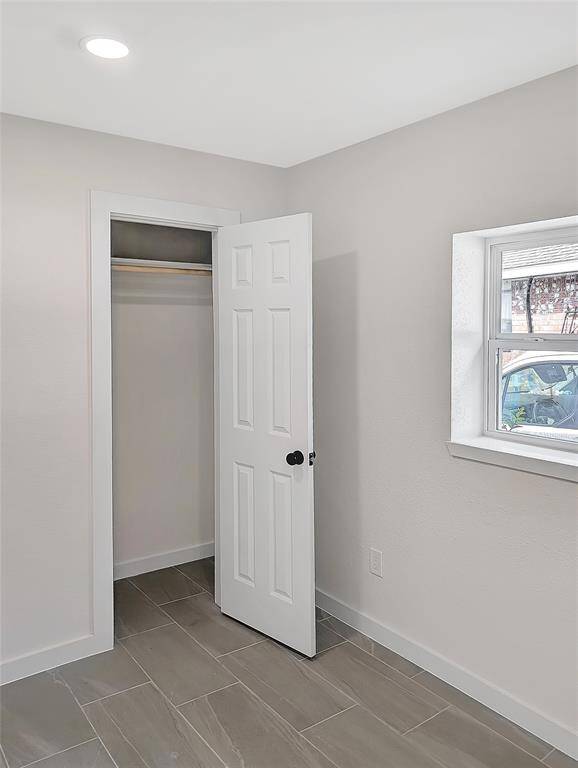This photo shows a small, bright room with neutral walls, a single window, a white door, and tiled flooring. Ideal for a home office or cozy bedroom.