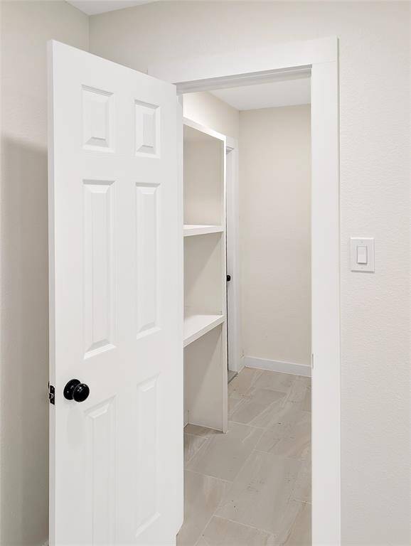 This is a compact laundry room featuring white cabinetry with black handles, plumbing hookups for a washer and dryer, and a neutral tile floor. There's a shelf for extra storage or folding space.
