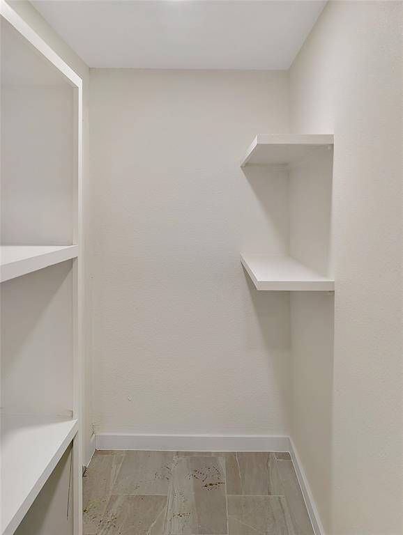 This room features a high ceiling with a modern beam, neutral tile flooring, and a large window with blinds, providing natural light and a spacious feel.