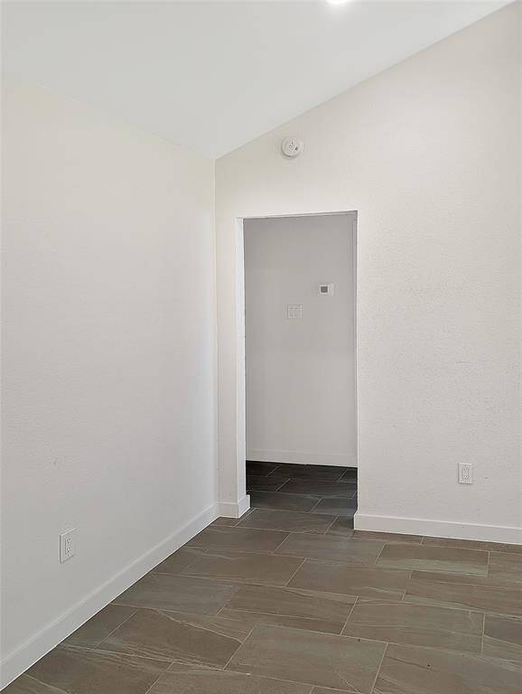 This photo shows a small, bright room featuring a closet with a white door, light gray tiled flooring, and a window providing natural light.