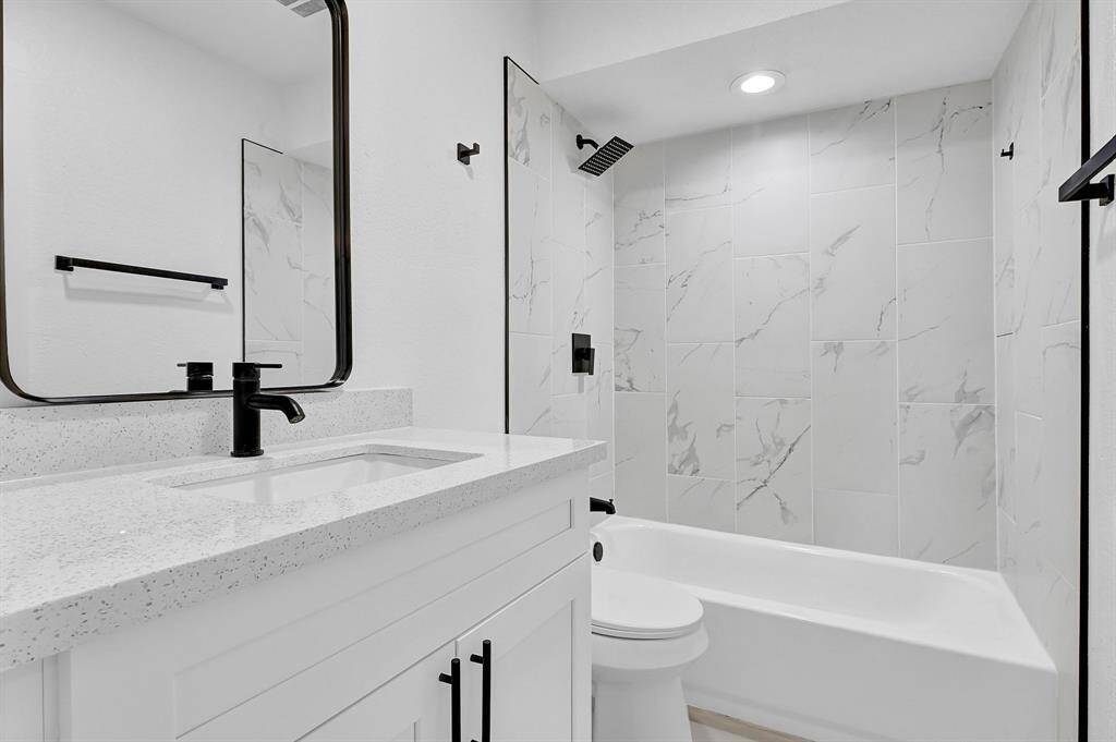 This modern bathroom features a sleek white vanity with black fixtures, a stylish rectangular mirror, and a unique octagonal window. The neutral tile flooring and light walls create a bright and airy atmosphere.