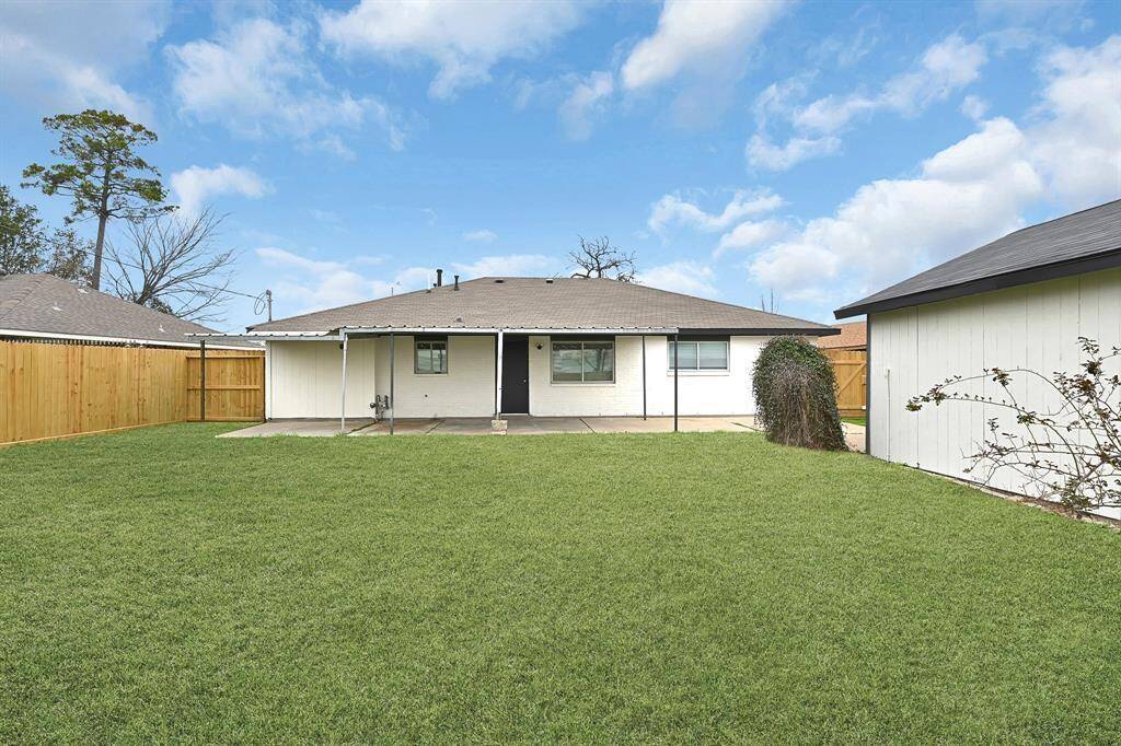 This photo showcases a spacious backyard with a neatly maintained lawn, a fenced perimeter for privacy, a small storage shed, and a covered patio attached to a single-story home, offering ample outdoor space for relaxation and activities.
