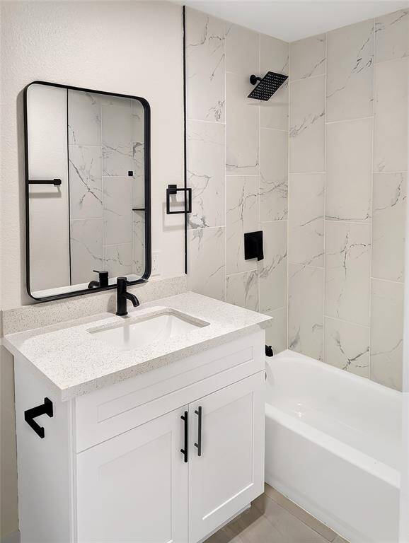 This photo showcases a bright, open-concept living area with modern tile flooring and recessed lighting. It features a sleek kitchen with white cabinetry and a black refrigerator, visible through a wide archway. The space is enhanced by a large window with blinds and a clean, minimalist design.