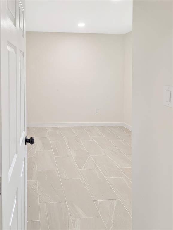 This photo shows a bright, modern interior with white walls and doors, recessed lighting, and wood-look tile flooring. The space includes a small alcove with shelves and a window with blinds, offering a clean and minimalist design.