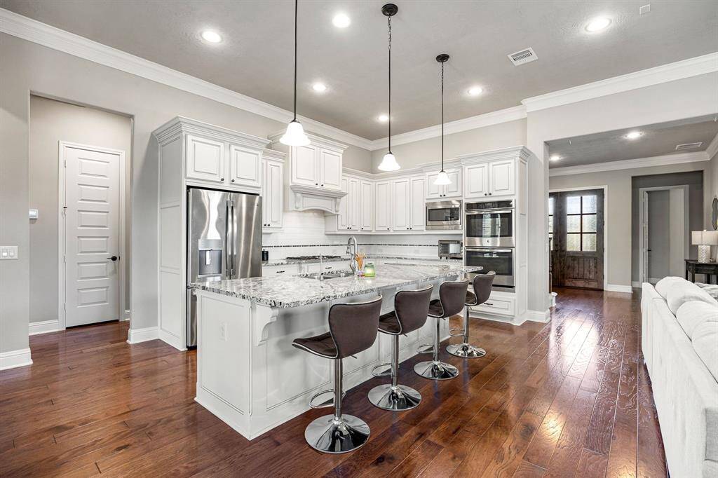 The chef’s kitchen boasts custom upgraded cabinetry, double ovens, stainless steel appliances, and a spacious breakfast bar with pendant lighting, perfect for casual dining or entertaining.