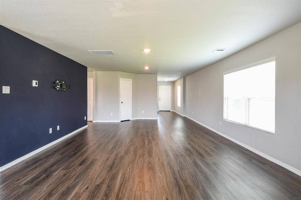 This exceptionally large living area is filled with abundant natural light. The front door can be seen at the rear of the image, highlighting the room's depth.