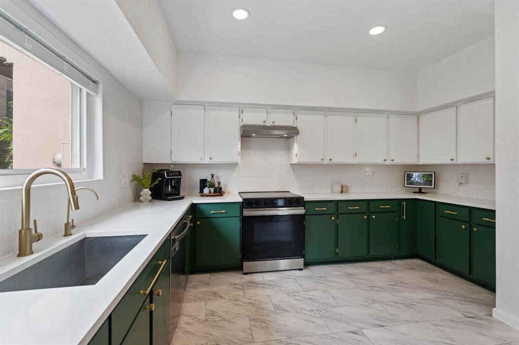 Guest half bathroom features a modern design with a sleek white quartz countertop, dark green cabinets, and gold hardware. It has a large, framed mirror and contemporary light fixtures, creating a stylish and inviting space.