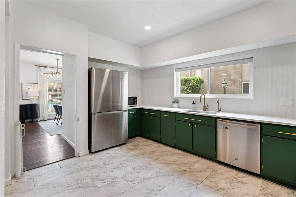 Kitchen features a modern design with sleek green lower cabinets and white upper cabinets. It includes stainless steel appliances, a large window for natural light, and elegant marble-patterned vinyl flooring, creating a bright and inviting space.