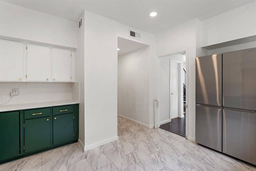 Kitchen features modern green lower cabinets with sleek brass handles, a central stainless steel dishwasher, and a wide window for natural light. The clean white quartz countertops and upper cabinets create a bright, inviting space.