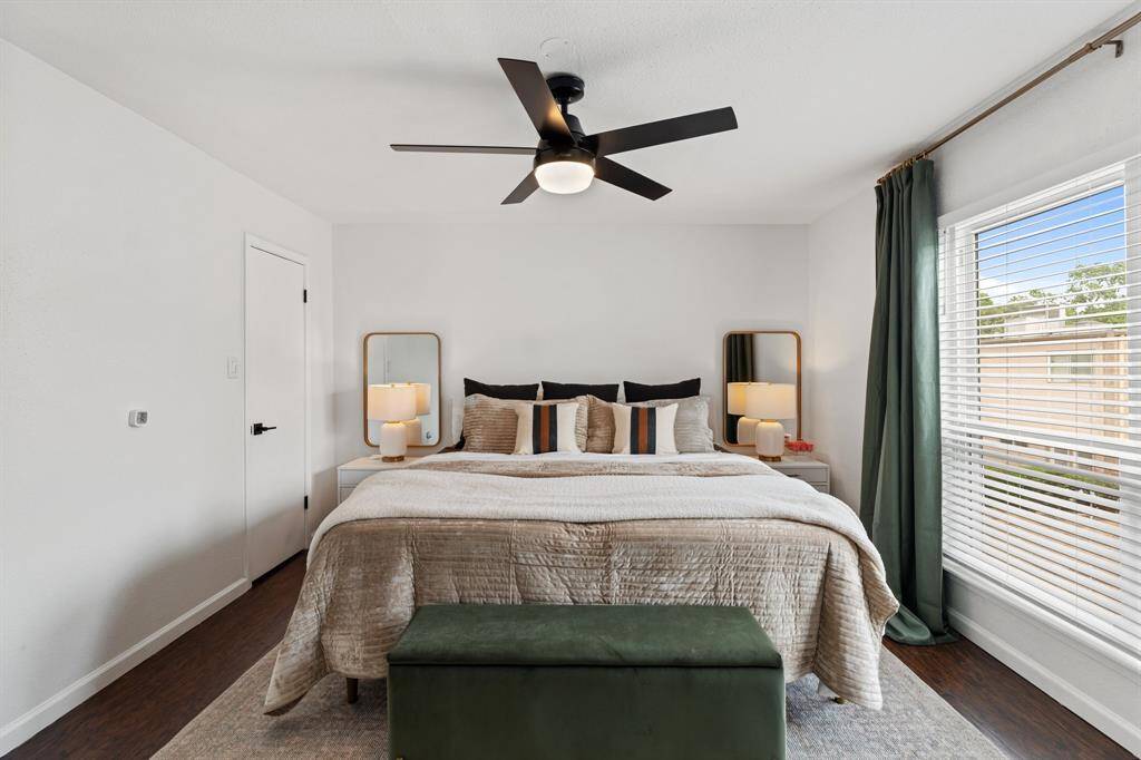 The modern kitchen features green lower cabinets with gold hardware and a sleek stainless steel dishwasher. It has a large window for natural light and opens into a dining area with elegant lighting.