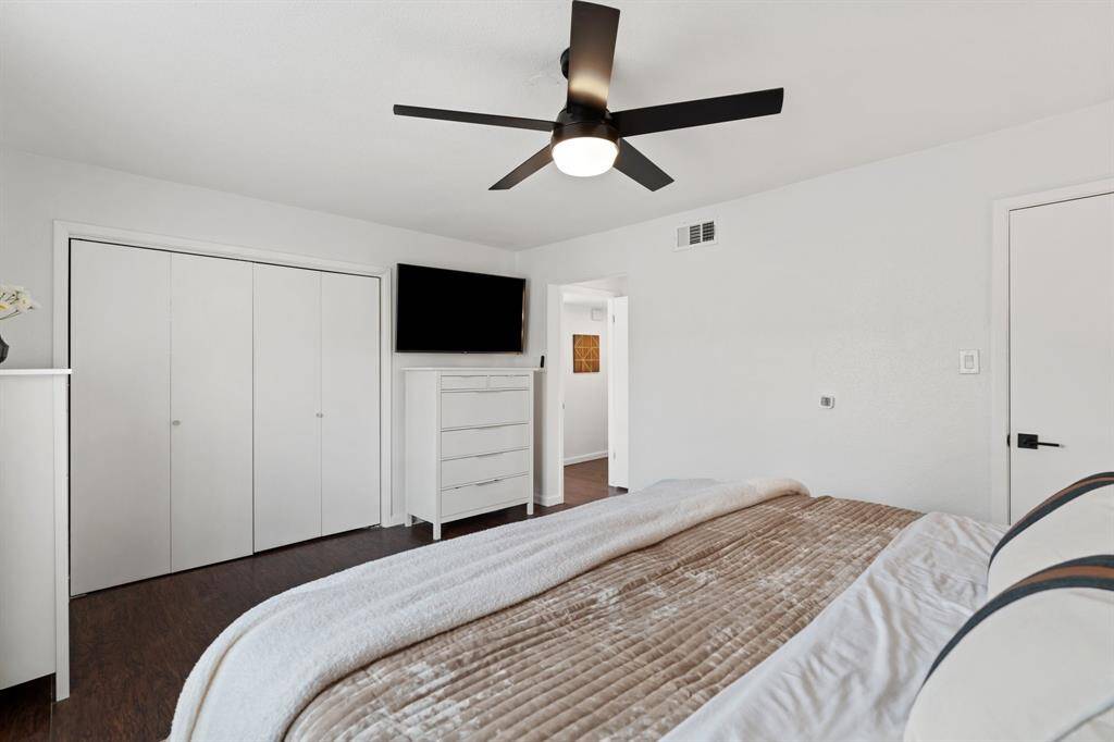 This primary bedroom is modern and inviting, featuring a clean white color scheme, a ceiling fan, laminate floors, and ample storage with a large closet and dresser. The room offers a comfortable and functional space.