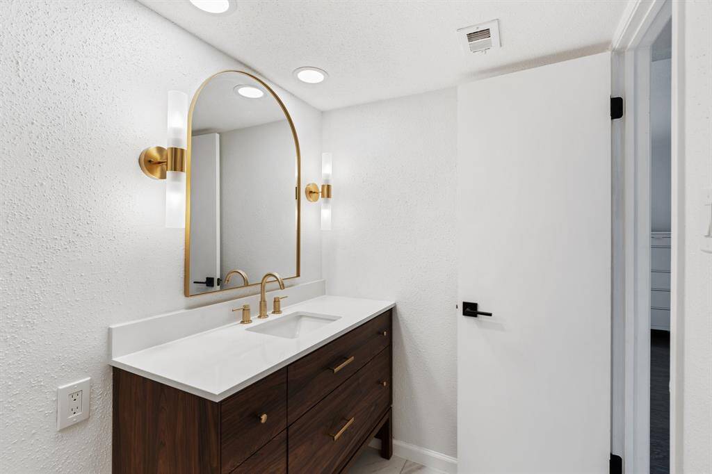 This modern bathroom features a sleek design with a glass-enclosed shower, green tile accents, and a stylish vanity. It includes a large mirror, contemporary lighting, and gold fixtures, creating a luxurious and inviting space.