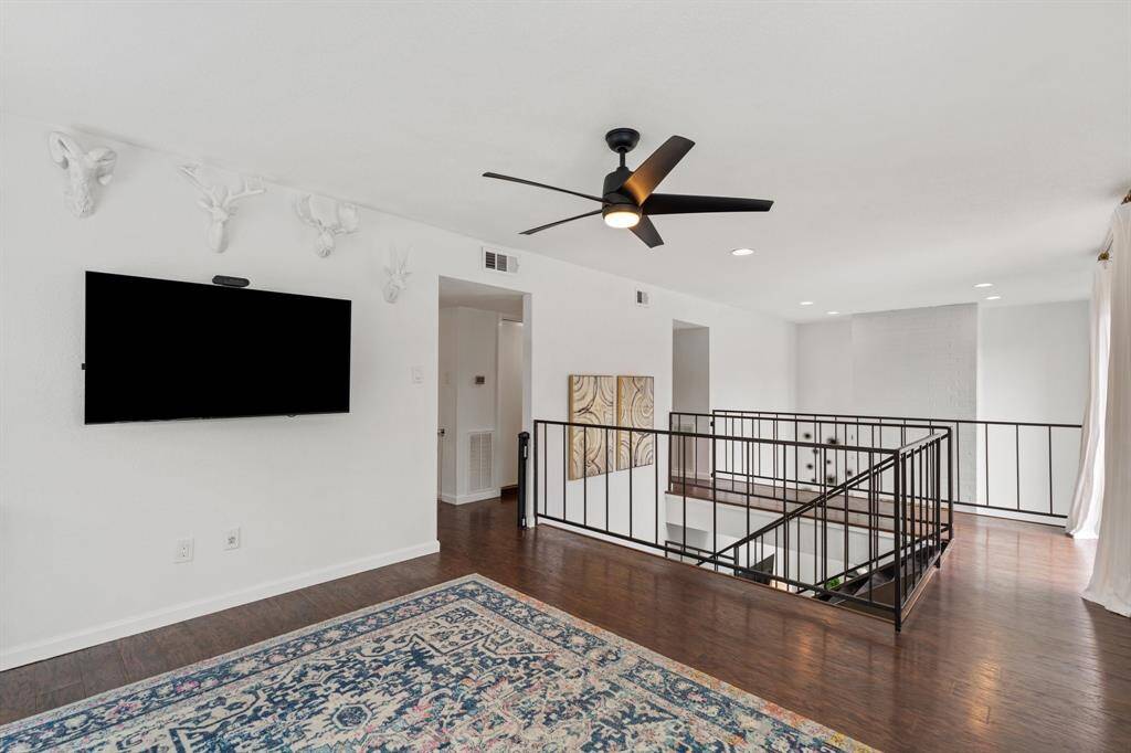 This open, airy loft space features laminate floors, a ceiling fan, and modern railings. A large window accents the space, providing a versatile area for relaxation or exercise.