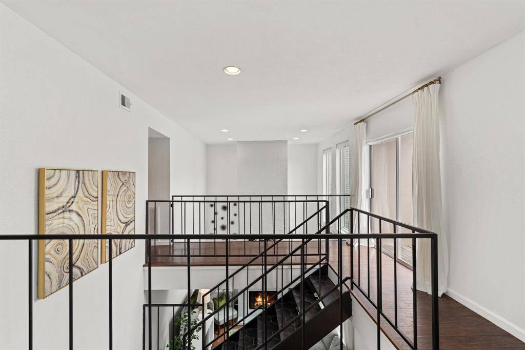 The modern living area upstairs features laminate floors and a ceiling fan. The space overlooks the lower level through a stylish black metal railing. Natural light filters in through large windows.