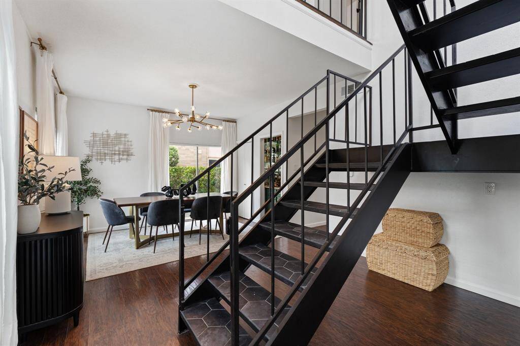This inviting living room features a high ceiling and abundant natural light from tall windows. It boasts a modern white brick fireplace and tasteful decor, creating a cozy yet elegant atmosphere perfect for relaxation and entertaining.