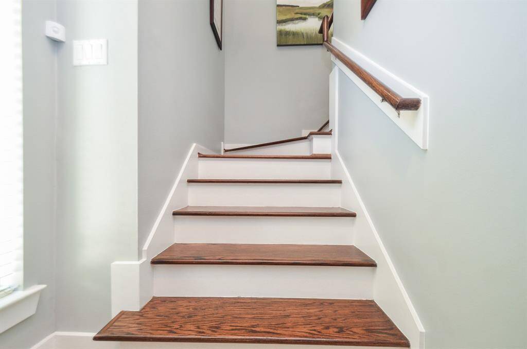 A well-lit, modern staircase with wooden steps and white risers, complemented by a sleek handrail. The walls are painted in a neutral tone, enhancing the clean and contemporary feel.