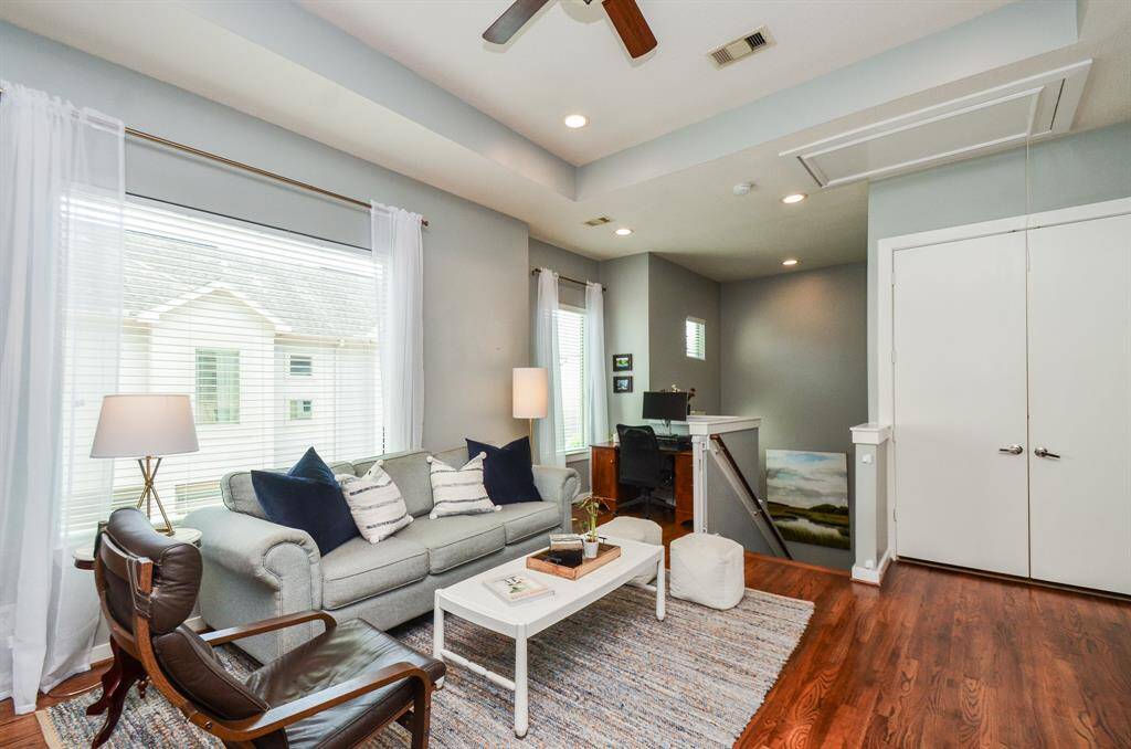 This inviting living/dining room features hardwood floors, natural walls, and a recessed ceiling with a ceiling fan. Abundant natural light, high ceilings, and tasteful decor create a warm, welcoming atmosphere.
