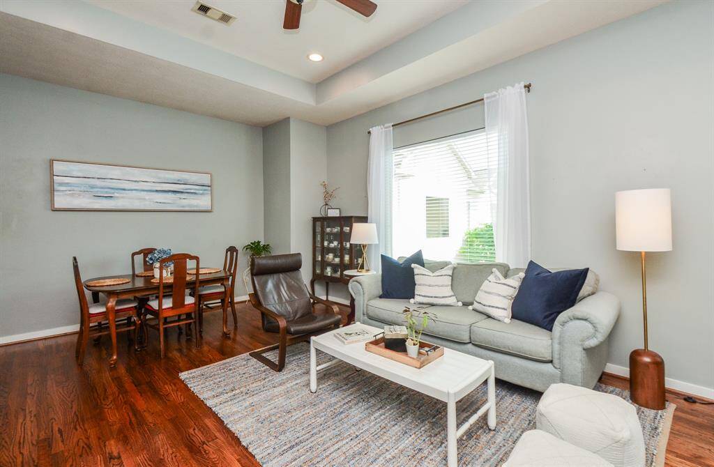 Bright and inviting living area with hardwood floors, neutral walls, and recessed lighting. Features a cozy seating area, large windows with natural light, and a small workspace. Ideal for relaxation and productivity.