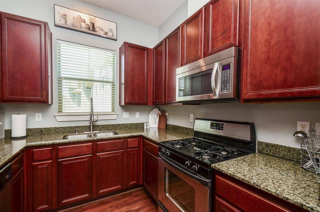 View of the abundance of granite countertops and rich wooden cabinets. It features stainless steel applicances, including a refrigerator and dishwasher. The space opens into a dining area with hardwood floors and ample natural light.