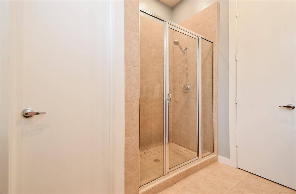 Primary bathroom features a modern glass-enclosed shower with light natural tiles, complementing the neutral-toned floor.