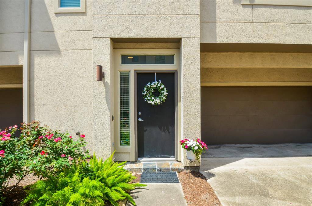 This photo showcases a modern entrance with a dark front door adorned with a decorative wreath. Flanked by sidelights, the entry is complemented by vibrant potted plants and a neat garden, offering a welcoming and stylish curb appeal.