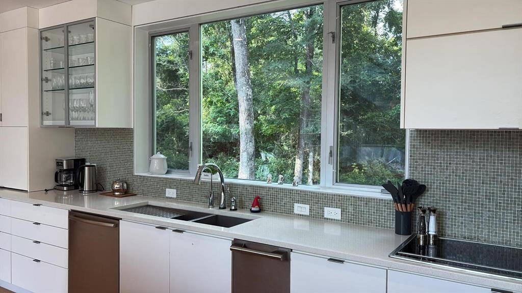 Expansive picture windows bring nature inside above a deep sink with modern fixtures and ample outlets.