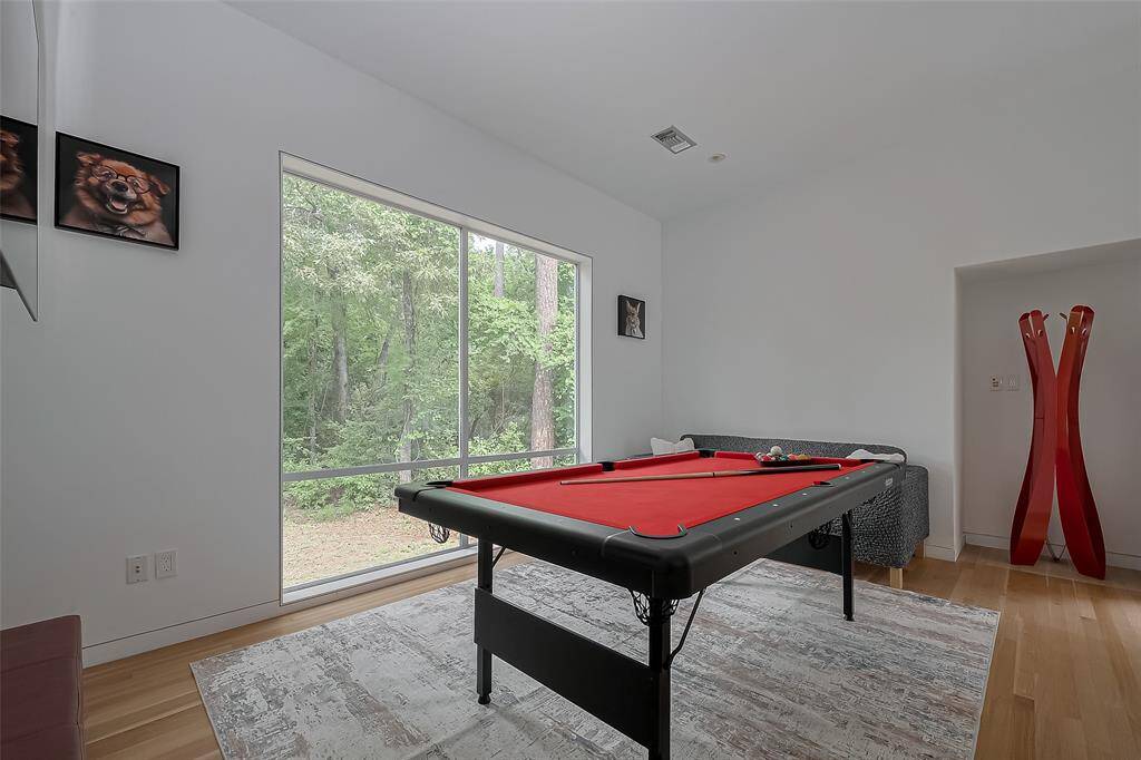 Versatile game room with a red-felt pool table and large windows overlooking the wooded backyard.