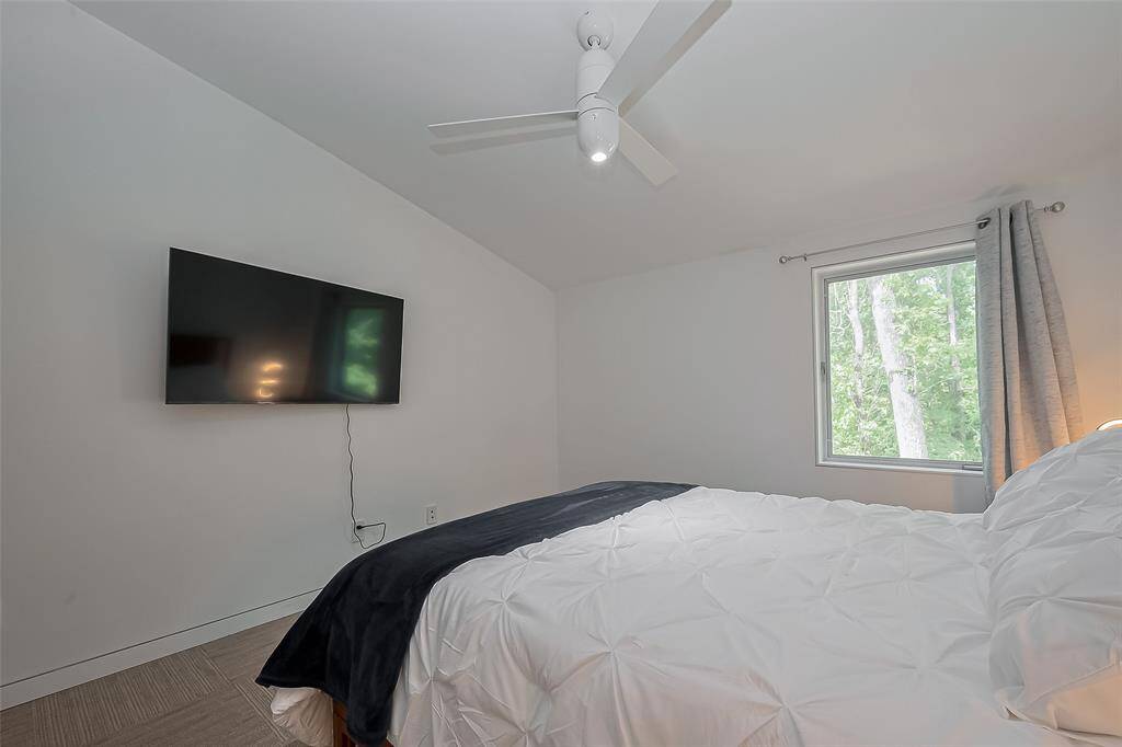 Tranquil bedroom retreat with mounted TV, tree-lined views, and minimalist design.