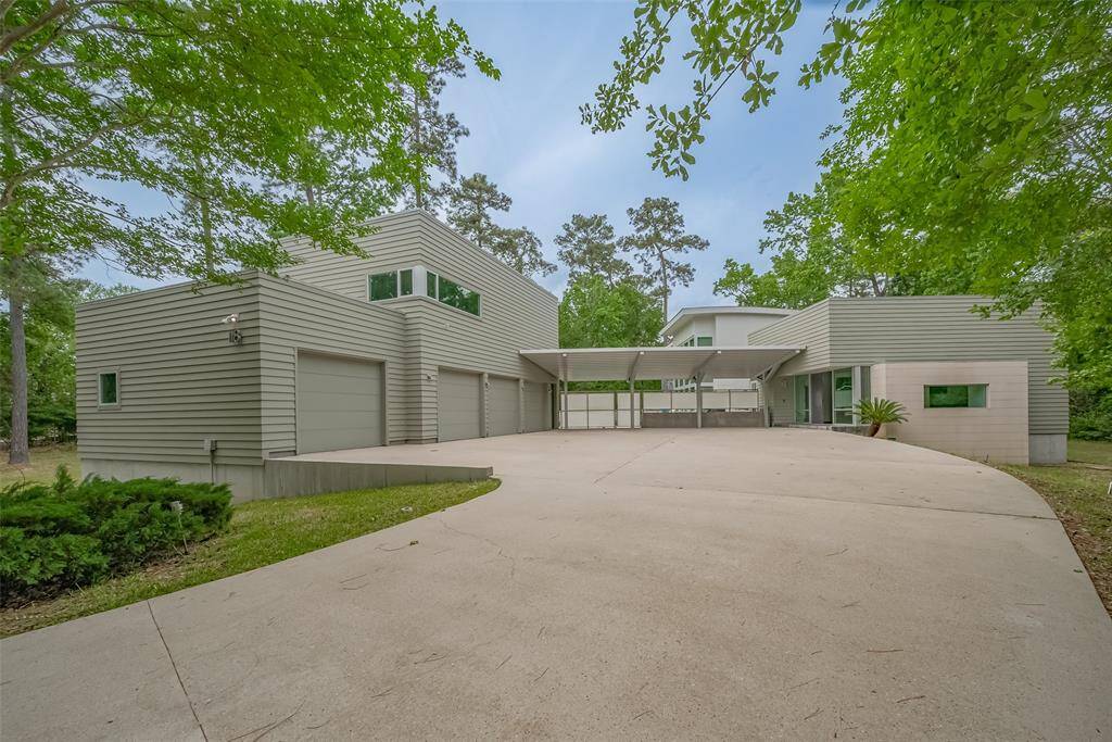 Sleek modern architecture with a gated entry, 4-car garage, and spacious driveway set on a wooded lot.