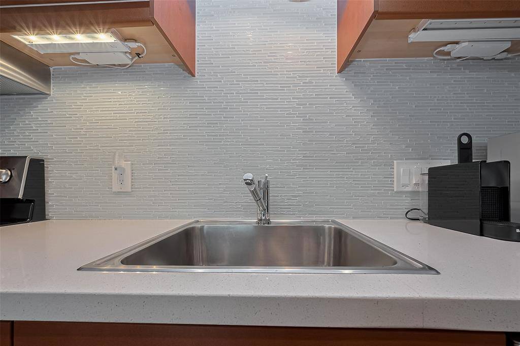Contemporary kitchen features a deep stainless-steel sink and detailed tile backsplash.