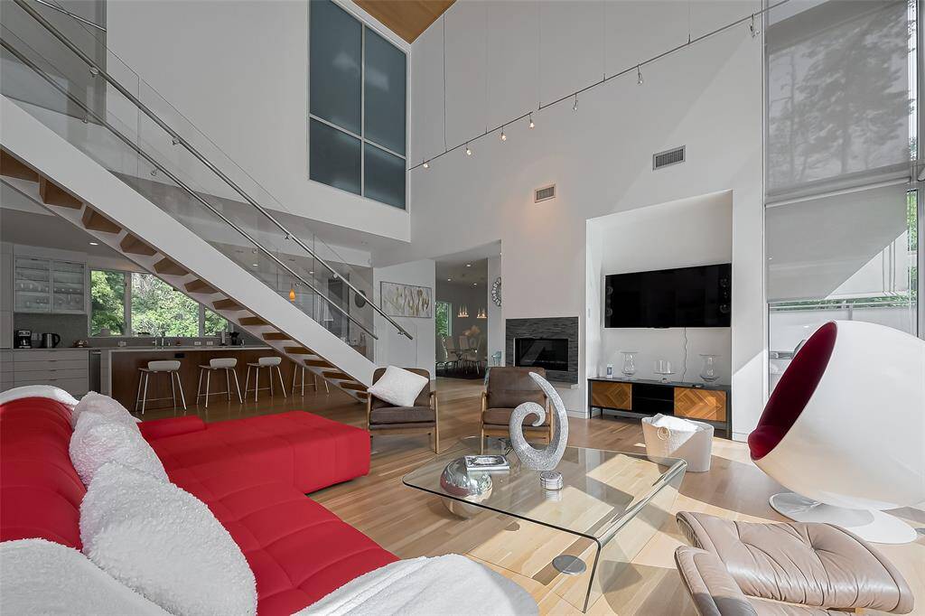 Stunning open-concept living room with soaring ceilings, a bold red sectional, and a sleek glass staircase that adds modern flair.