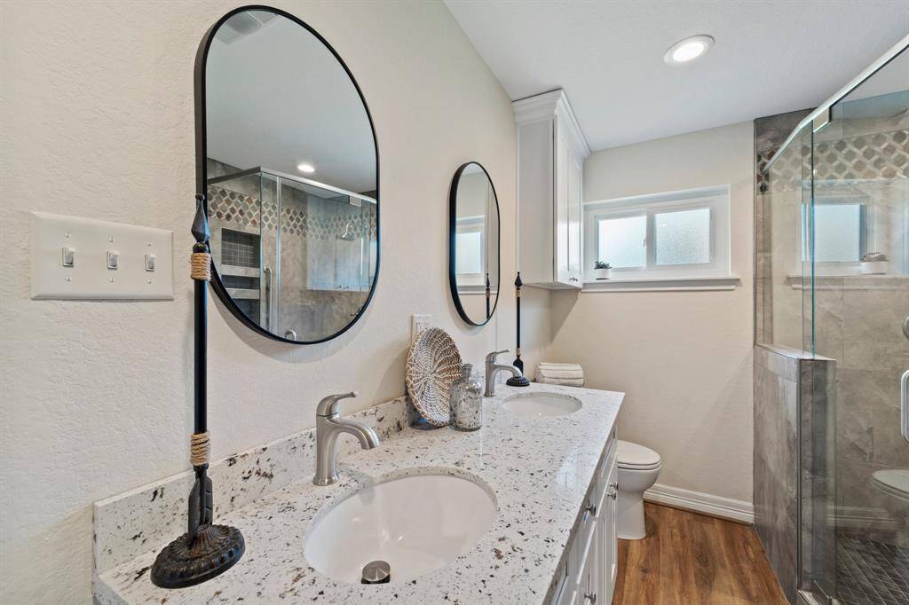 This elegant bathroom features a modern granite countertop, ample storage, and a stylishly tiled shower with built-in shelving. Perfect for a refreshing start to your day.