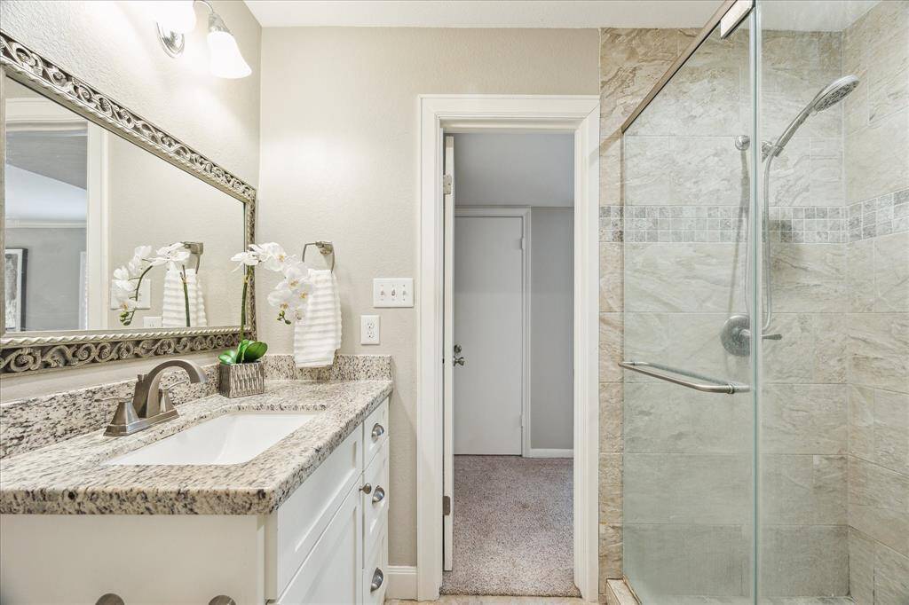 The en suite bath offers a granite-topped vanity, updated lighting, and a frameless glass shower with stone tile surround.
