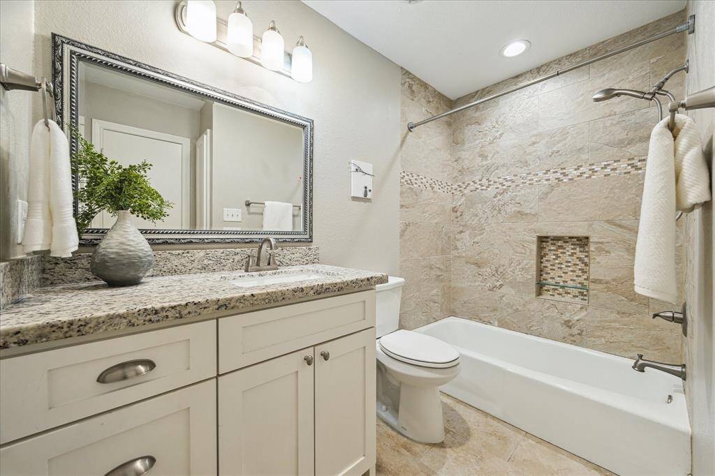 The upstairs full bath features granite counters, updated lighting, and a tiled tub/shower surround with built-in niche.