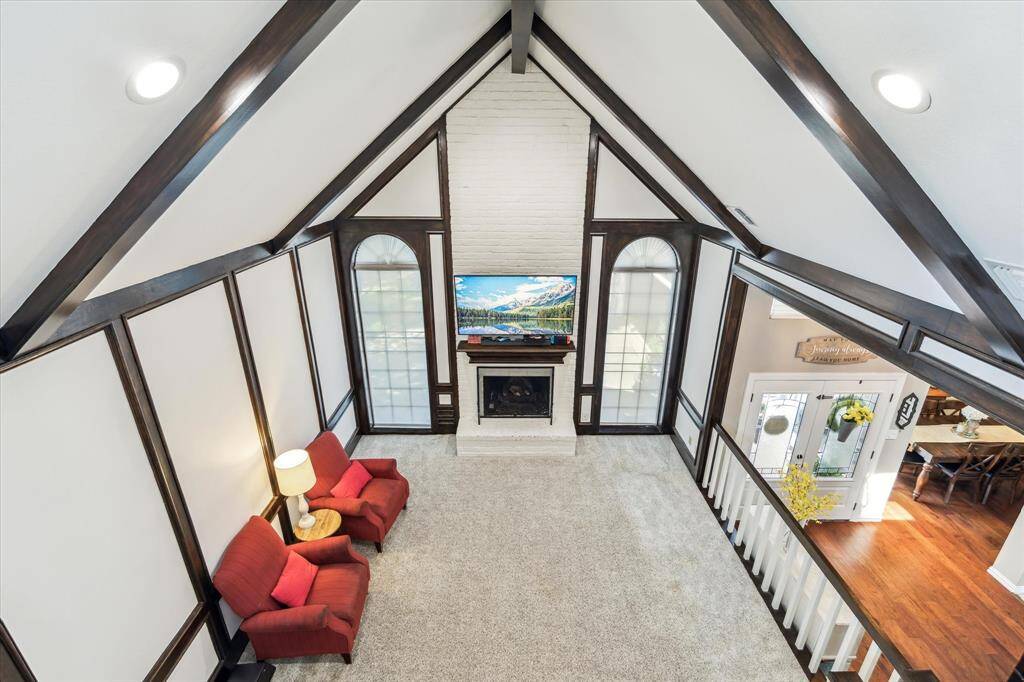 View from the upstairs game room showcases the dramatic transformation in the living area—stained wood walls, ceiling beams, and stair rails in a darker tone, beautifully contrasted by crisp white painted panels, creating a modern aesthetic.