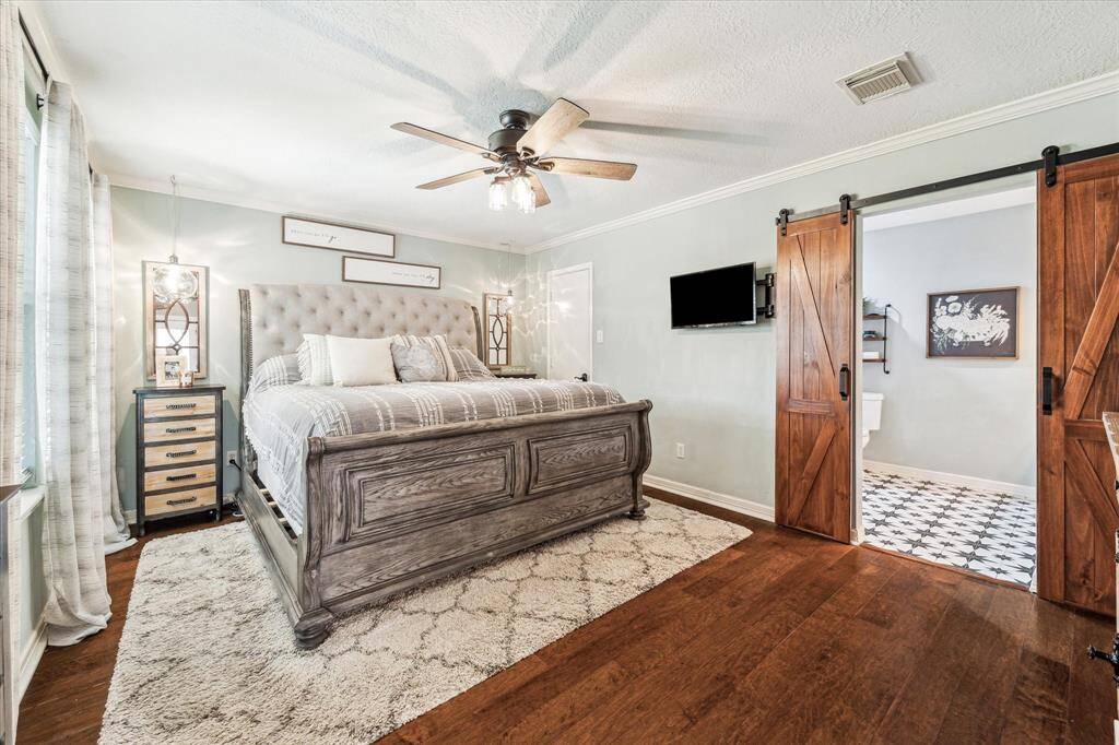 The primary bedroom featuring all-new engineered hardwood flooring and a modern barn door that offers access to the en-suite bathroom. A new ceiling fan upgrades throughout the home.