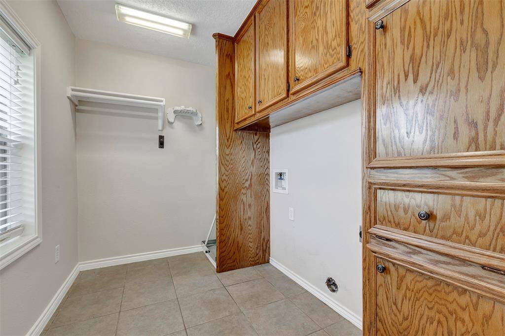 This space is designed for a laundry area, with electric washer and dryer connections and ample cabinets for laundry supplies.