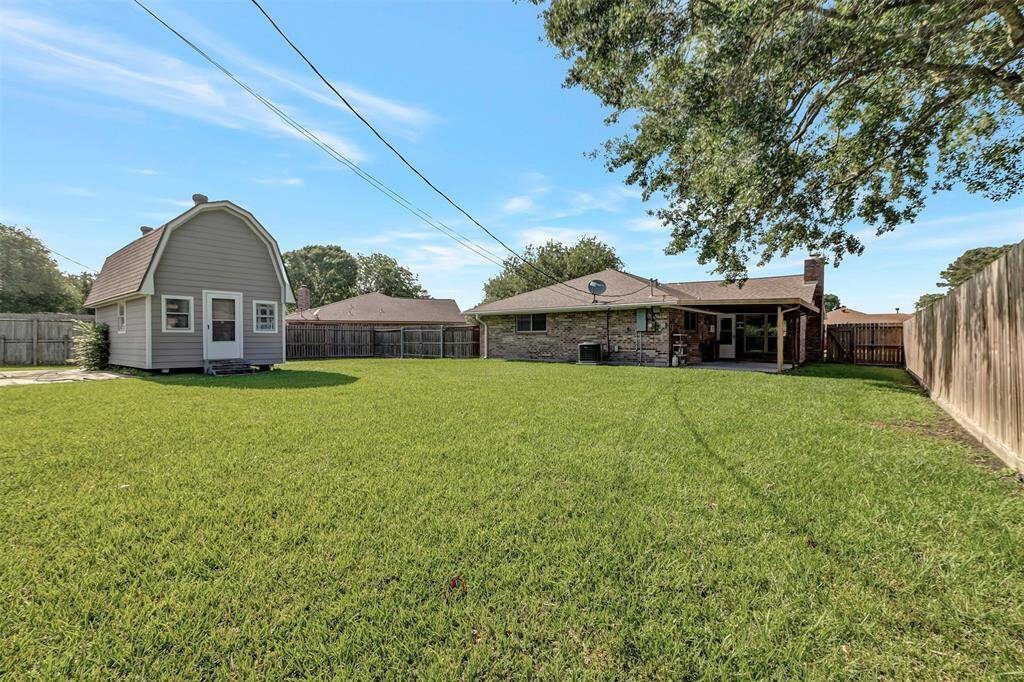 A wider view of the fully fenced, spacious backyard showcases the grass-covered lawn and a convenient storage shed.