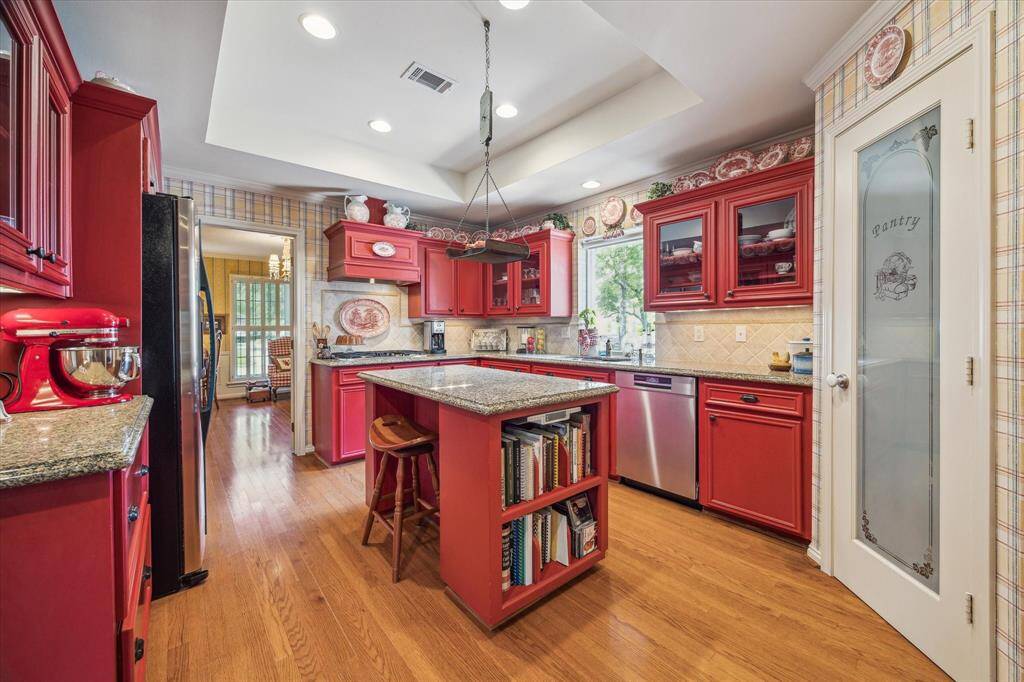 A central island with bar seating invites casual dining and cook book storage, while double ovens and a gas cooktop make it a chef’s dream. The tray ceiling adds depth and character, enhancing the overall charm of the space.