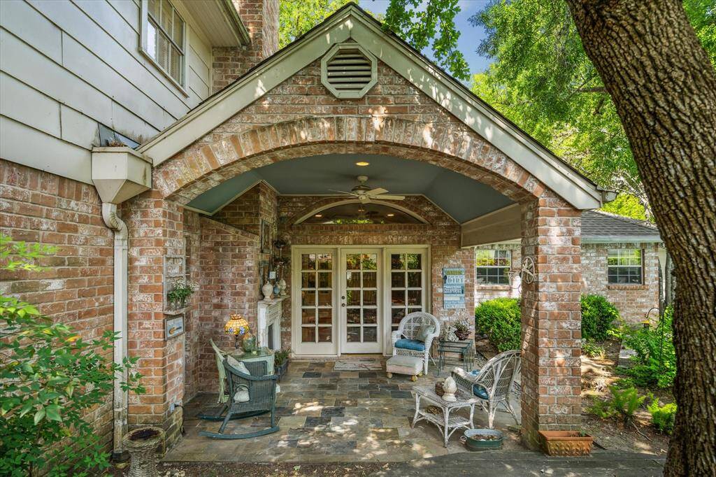 The back patio features a tongue-and-groove ceiling that adds warmth and character overhead. A decorative faux fireplace creates a cozy focal point, while the surrounding shaded gardens offer a peaceful, private setting for relaxing or entertaining outdoors.
