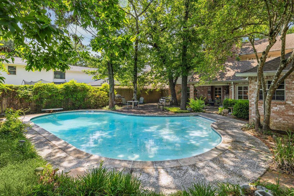 The backyard offers a picturesque view looking back toward the house, showcasing the inviting pool, expansive deck, and charming covered patio. Framed by lush landscaping and mature trees, this beautifully designed outdoor space is ideal for both lively gatherings and peaceful moments at home.